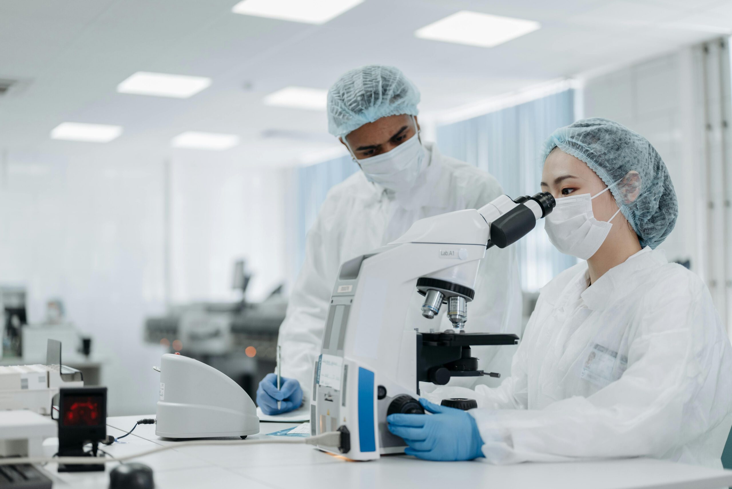 Two scientists-- male and female-- in a lab, the female scientist looking into a microscope.